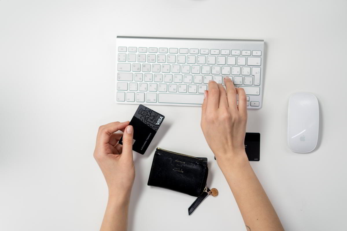 Eine Frau wechselt nahtlos ihr digitales Girokonto, während sie auf einer Tastatur tippt und eine Brieftasche und eine Kreditkarte in der Hand hält.