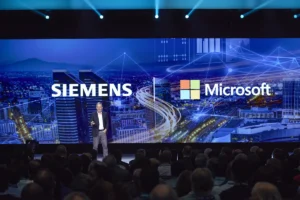 Ein Moderator steht auf der Bühne vor einem großen Bildschirm, auf dem die Logos von Siemens und Microsoft zu sehen sind, und spricht zu seinem Publikum. Im Hintergrund ist eine futuristische Stadtlandschaft mit Lichtspuren zu sehen, die das Potenzial von KI-gestütztem PLM bei der Transformation moderner Industrien hervorhebt.