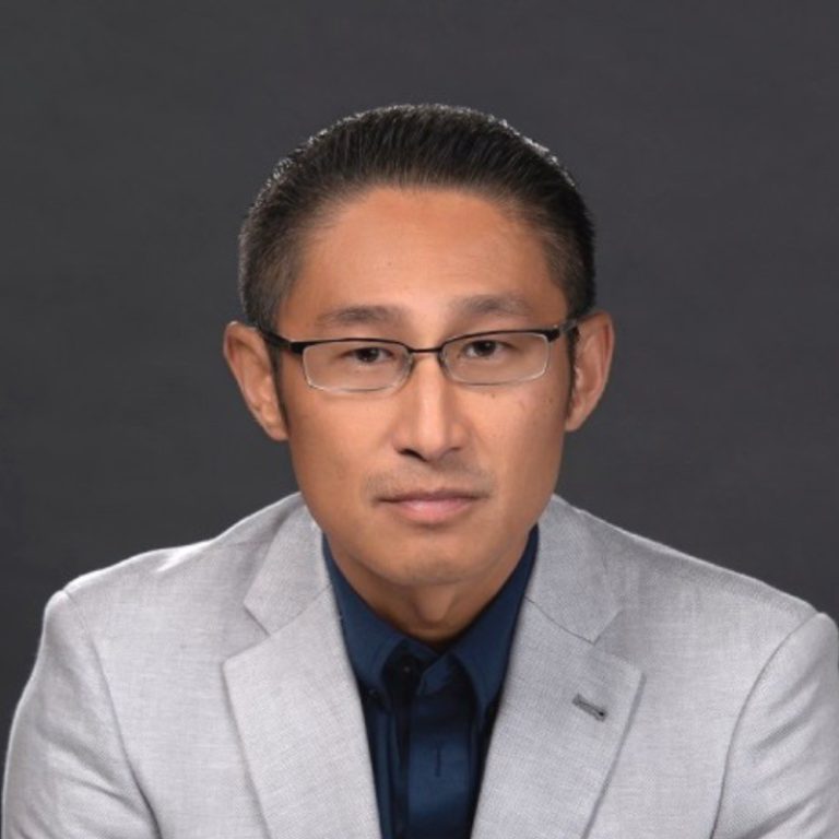 Joseph Kim mit kurzen dunklen Haaren, der eine Brille, einen hellgrauen Blazer und ein dunkles marineblaues Hemd trägt, sitzt vor einem schlichten dunklen Hintergrund und blickt mit neutraler Miene in die Kamera - er repräsentiert die innovative Agentic AI-Plattform von DRUID AI.