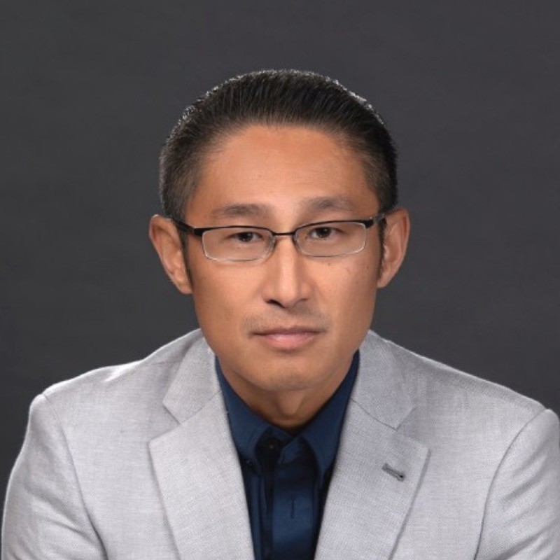Joseph Kim mit kurzen dunklen Haaren, der eine Brille, einen hellgrauen Blazer und ein dunkles marineblaues Hemd trägt, sitzt vor einem schlichten dunklen Hintergrund und blickt mit neutraler Miene in die Kamera - er repräsentiert die innovative Agentic AI-Plattform von DRUID AI.