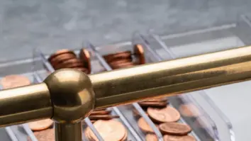 Kupferne Kostentoken sammeln sich in festen transparenten Sichtschalen hinter einer versiegelten Messingschiene.
