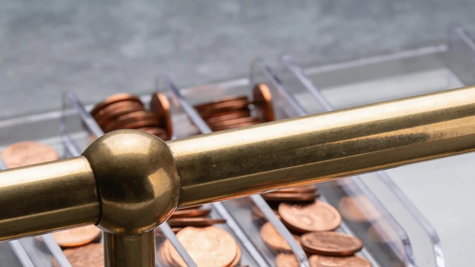 Kupferne Kostentoken sammeln sich in festen transparenten Sichtschalen hinter einer versiegelten Messingschiene.