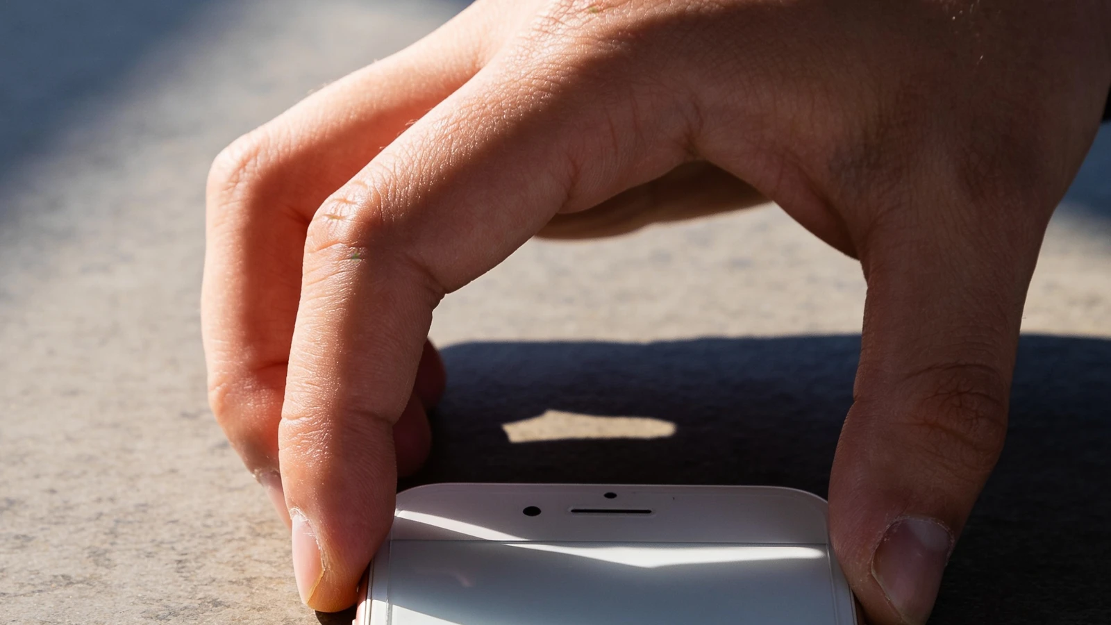 Eine Hand greift nach einem Smartphone auf einer steinernen Oberfläche.