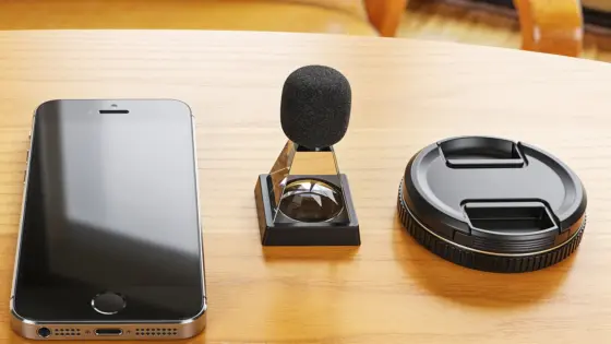 Ein Smartphone liegt neben einem kleinen Mikrofon und einer Kamerakomponente auf hellem Holz.