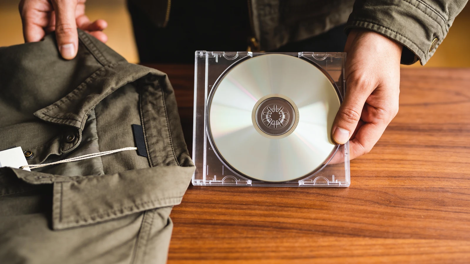Eine Hand ordnet die Farbe und Struktur einer Secondhand-Jacke einer transparenten Musikscheibe zu.
