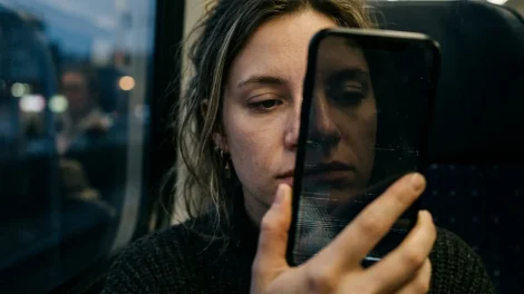 Deepfakes erkennen – Gesicht in dunklem Smartphone-Bildschirm reflektiert mit digitaler Verzerrung